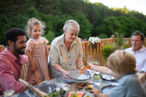 A multigenerational family sitting down for dinner on a patio outside on a beautiful summer evening