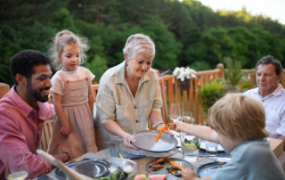 A multigenerational family sitting down for dinner on a patio outside on a beautiful summer evening