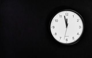 A white-faced clock hanging on a black wall