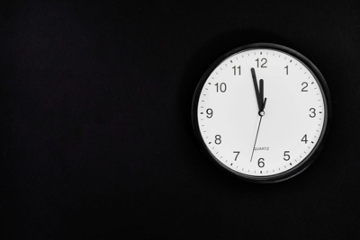 A white-faced clock hanging on a black wall