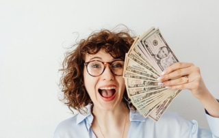 A young woman holding a stack of cash and smiling.