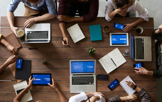A group of professionals collaborating at a large desk with various devices.