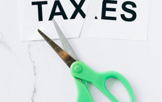 A piece of paper with the word "taxes" printed on it, cut in half next to a pair of scissors.