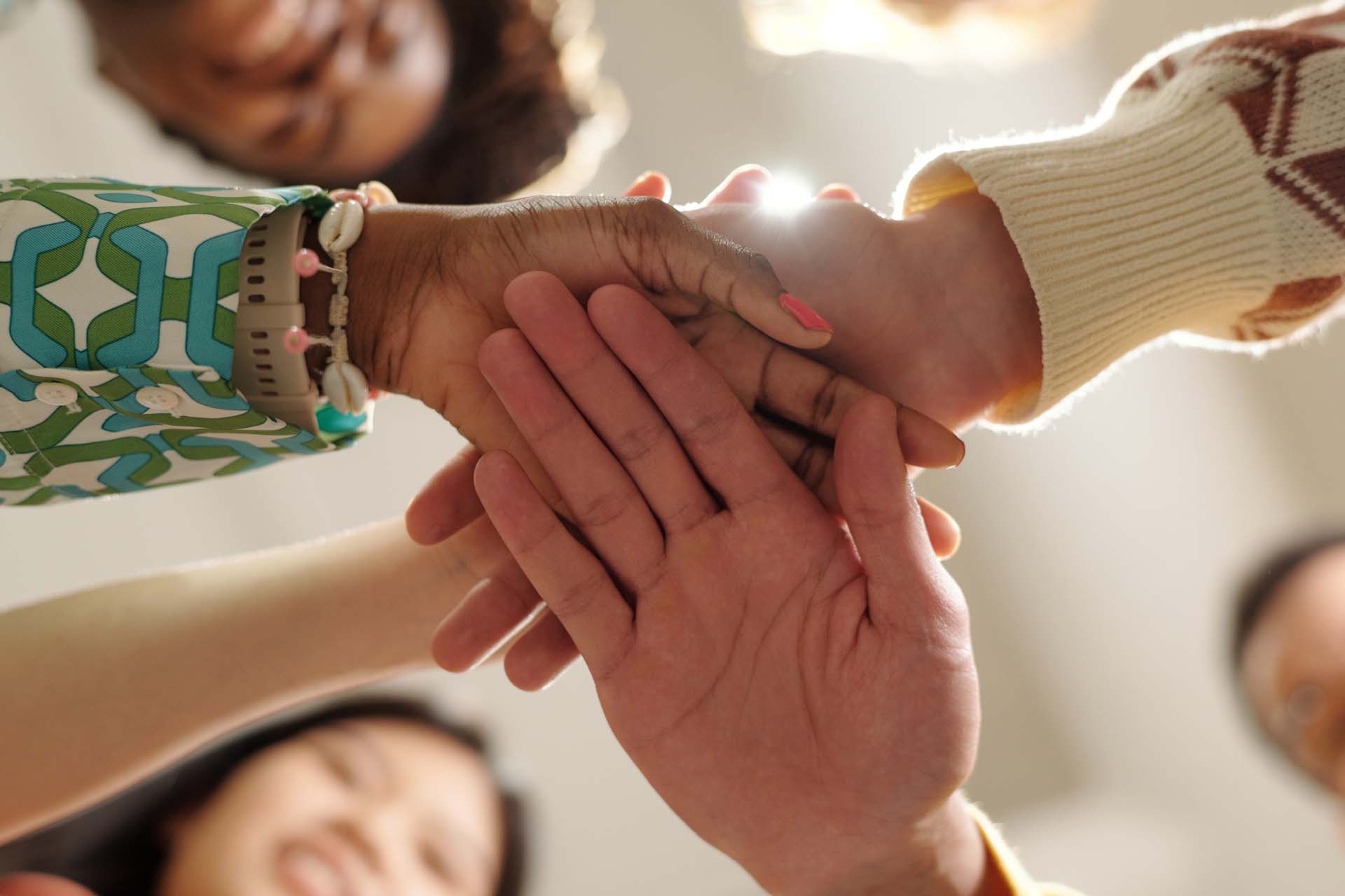 Diverse group of young adult and middle aged men and women stacking hands in creative coworking space, showing close up of Caucasian, Black, and Asian hands joining together
